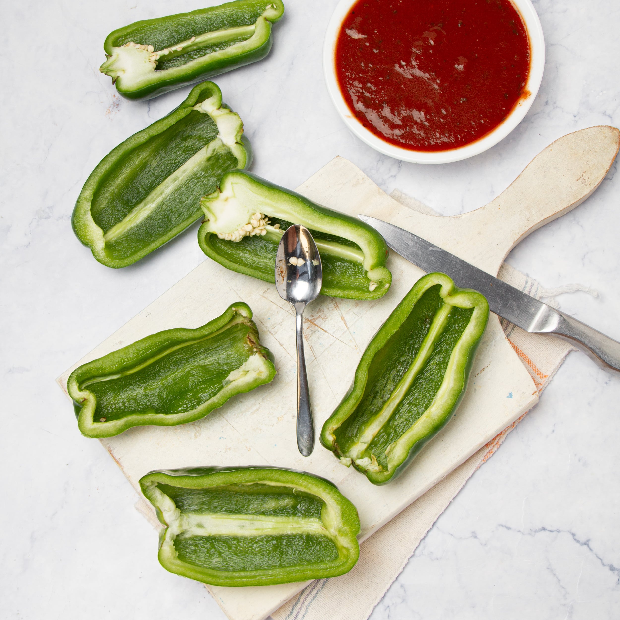 Poblano peppers halved lengthwise and hollowed out on a cutting board, next to a bowl of red enchilada sauce.