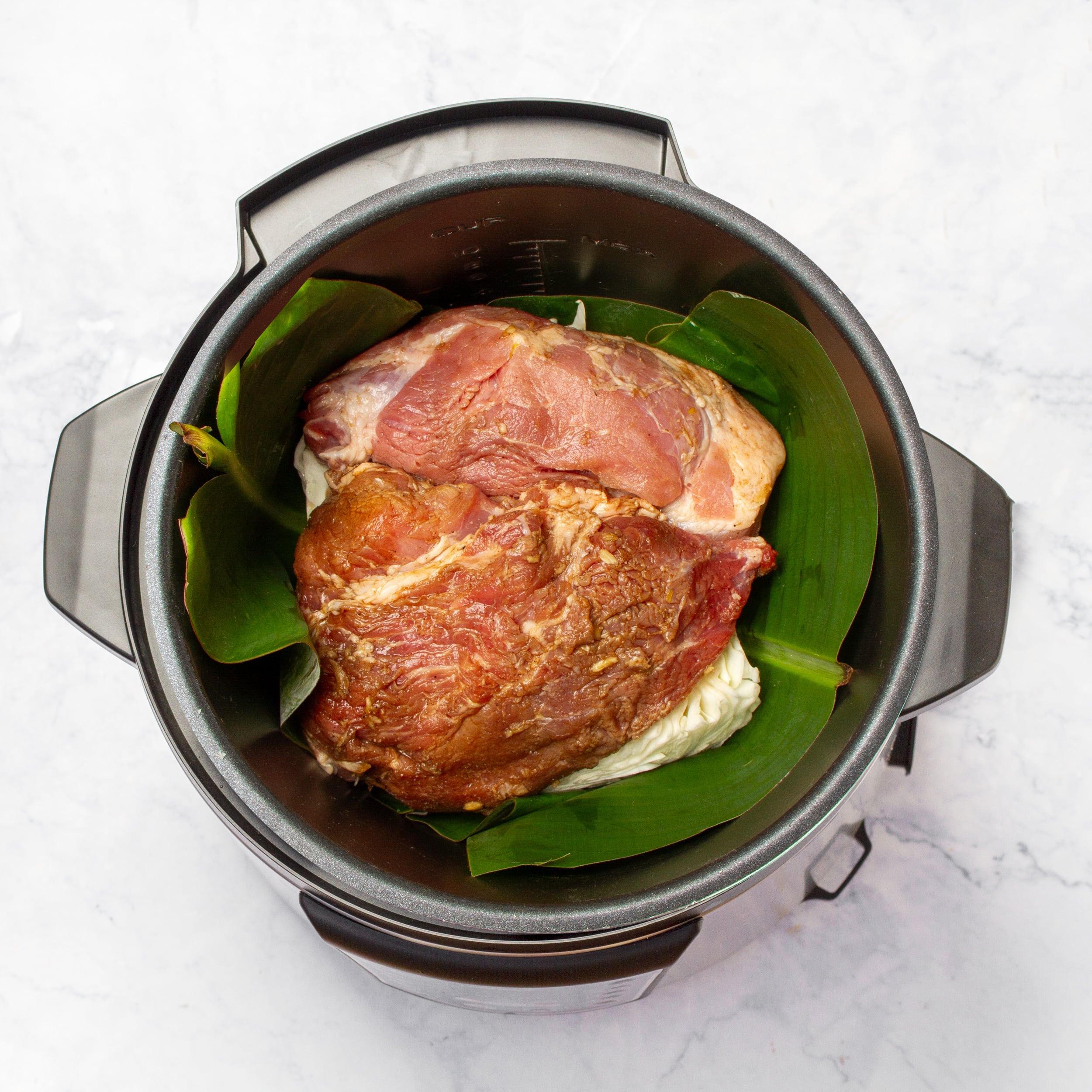 Seasoned pork shoulder set on top of the cabbage and banana leaves in the slow cooker.