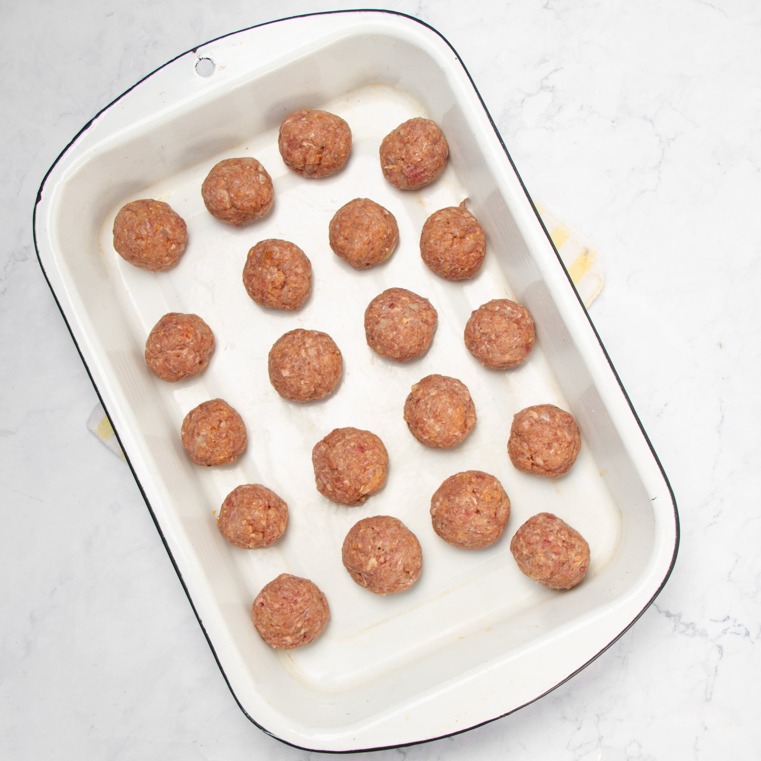 Meatballs rolled and placed in a baking dish. 