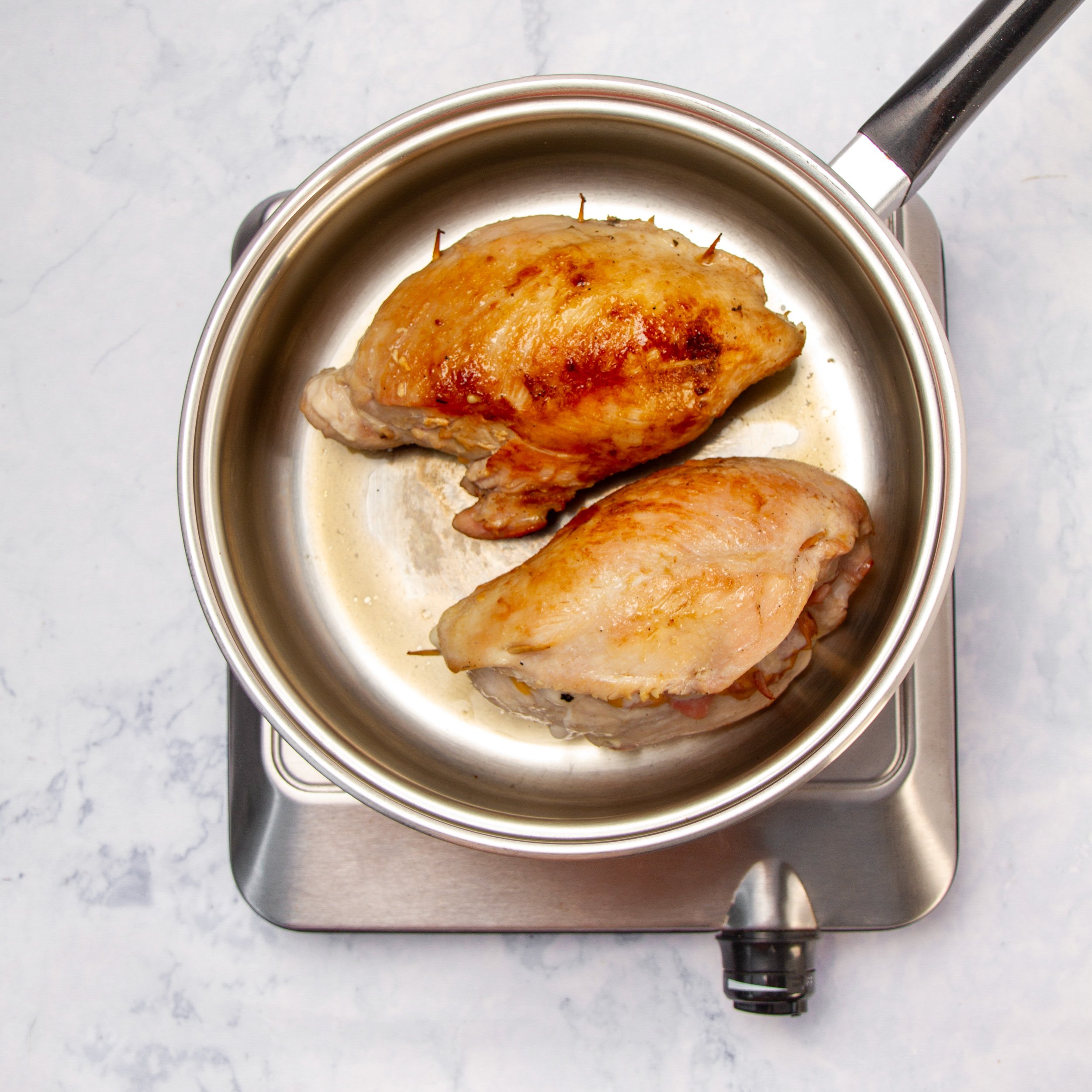Stuffed chicken breasts cooking in a hot pan.