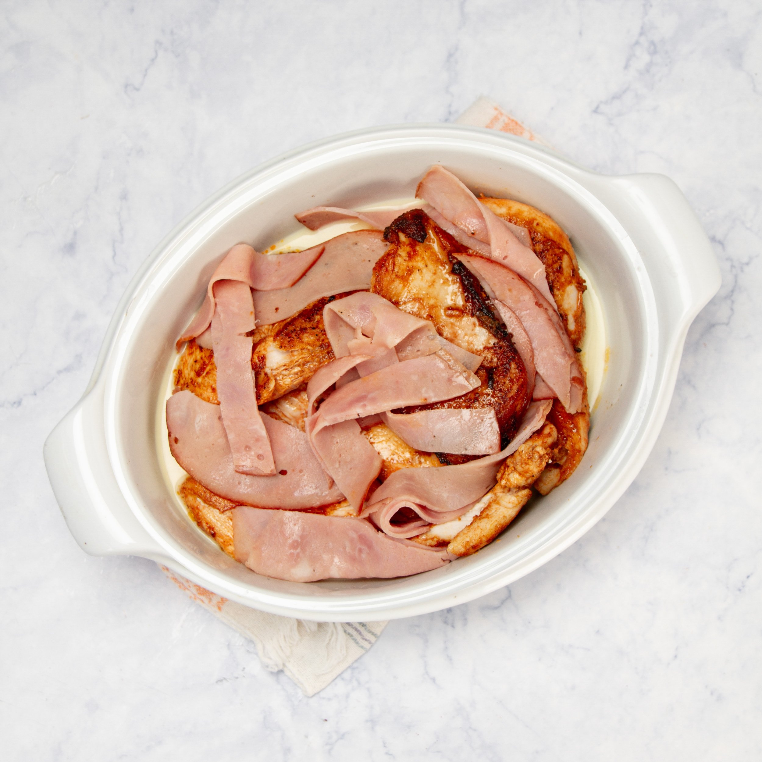 Cooked chicken breasts and ham layered in the baking dish.