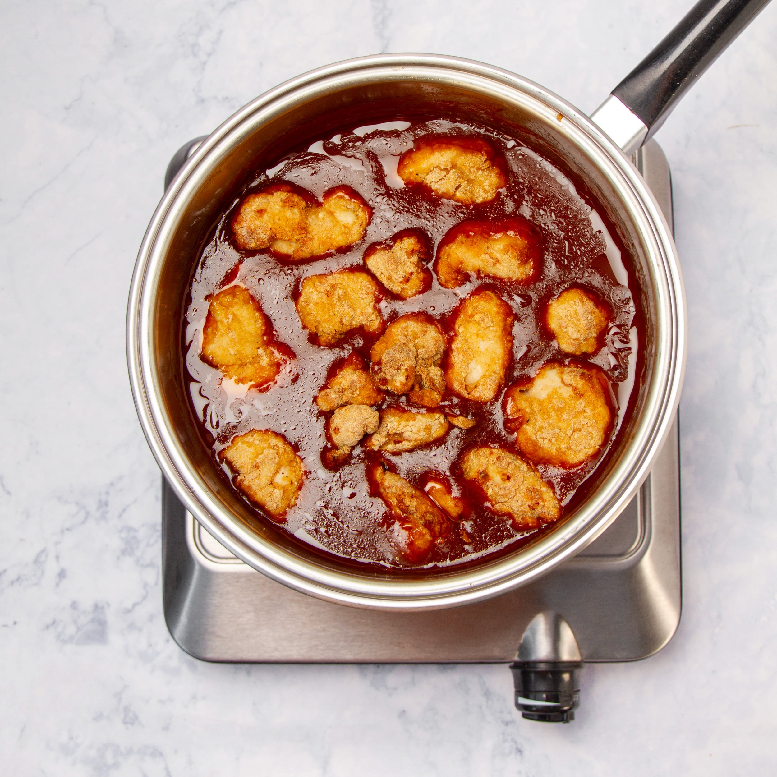 Crispy chicken bites cooking in the sauce in a pot. 