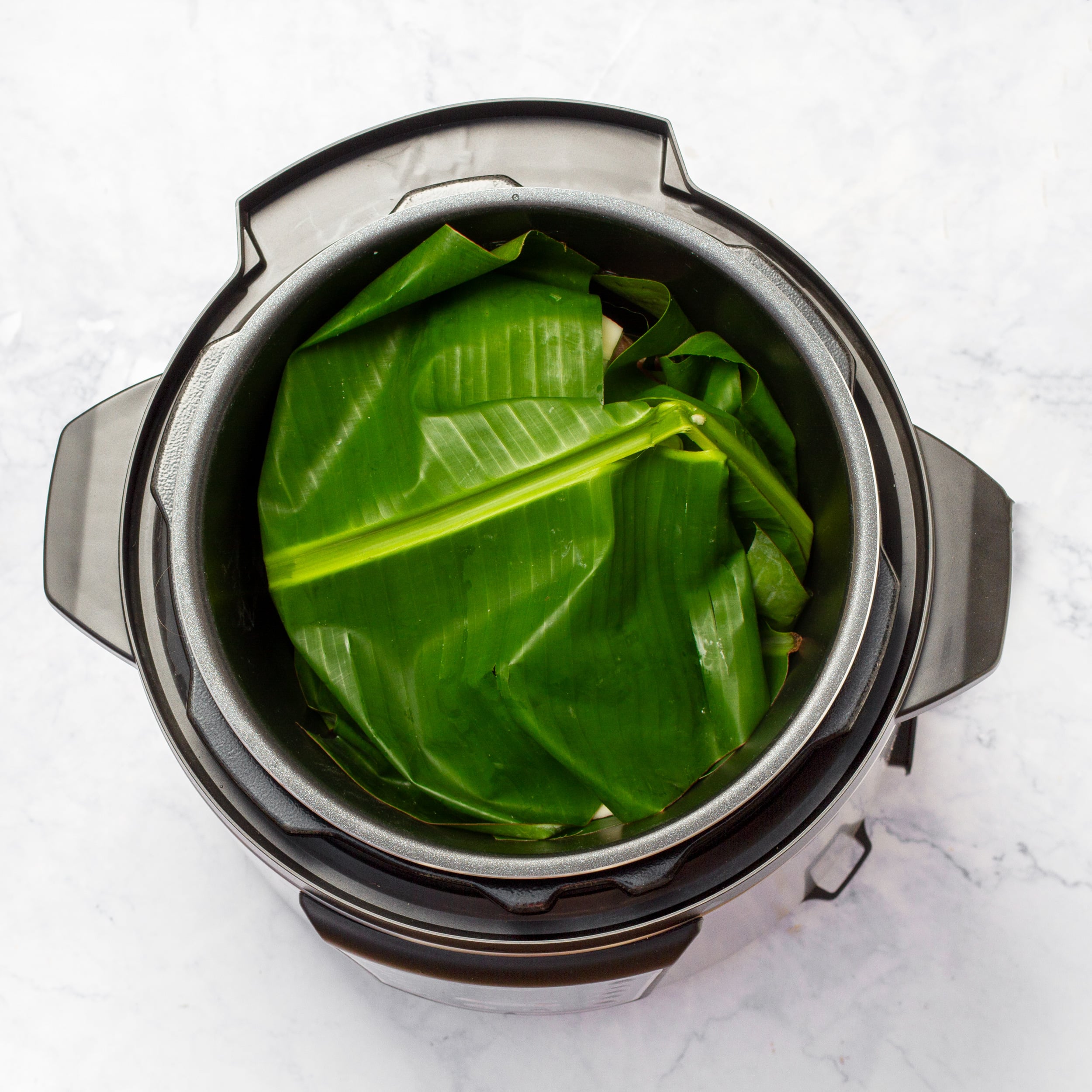 The banana leaf ends closed on top of the meat and veggies in the slow cooker pot. 