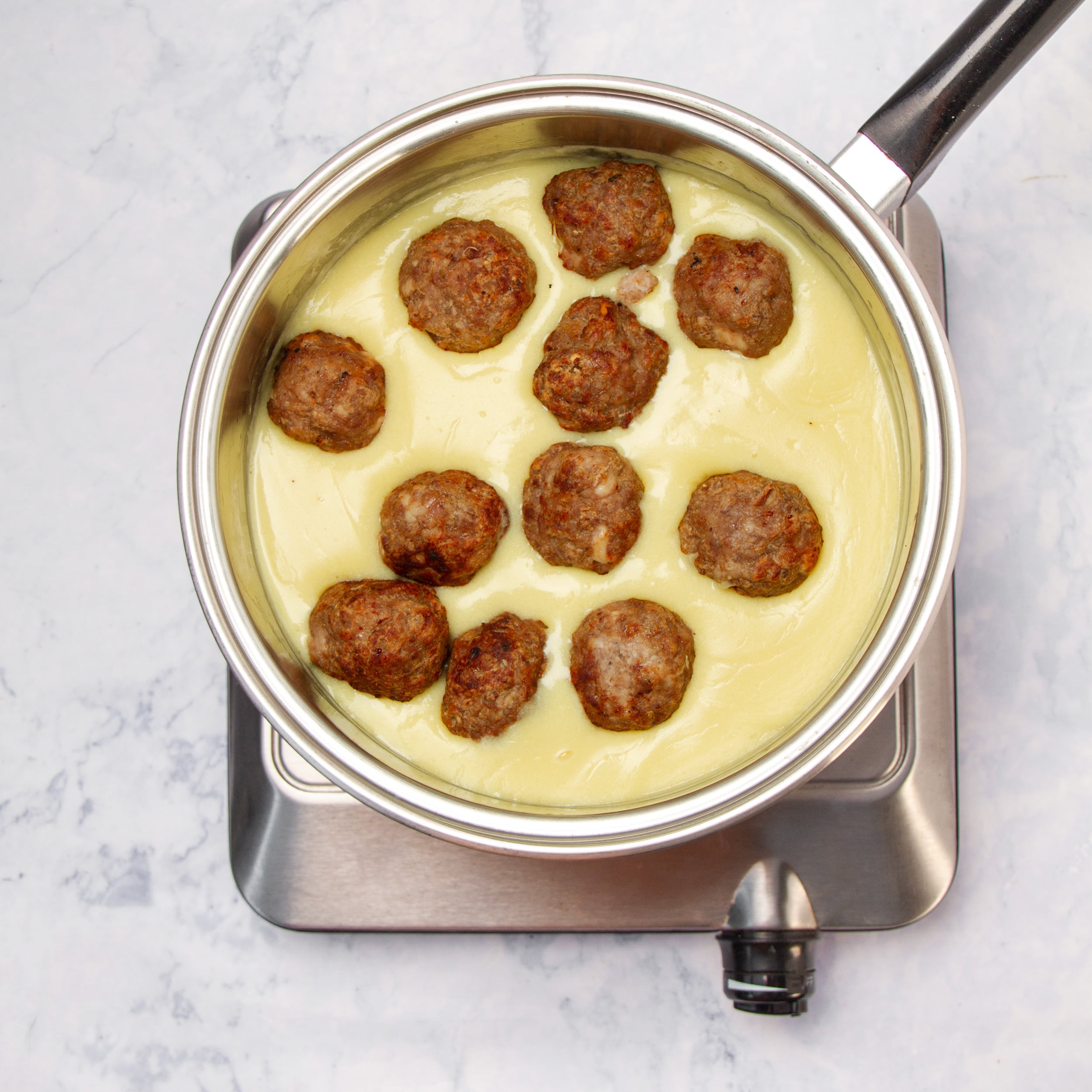 Cooked meatballs added to a saucepan with the creamy yogurt sauce. 