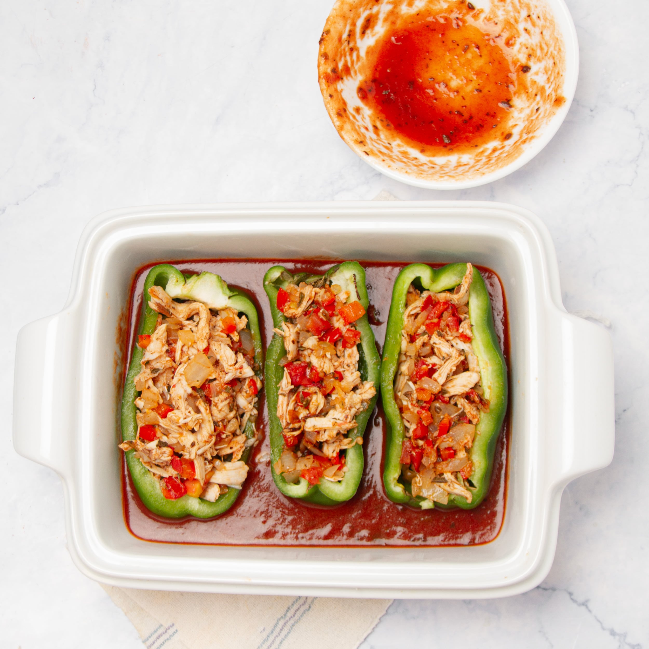 Poblano halves filled with the chicken enchilada mixture in a bed of enchilada sauce, ready for the oven.
