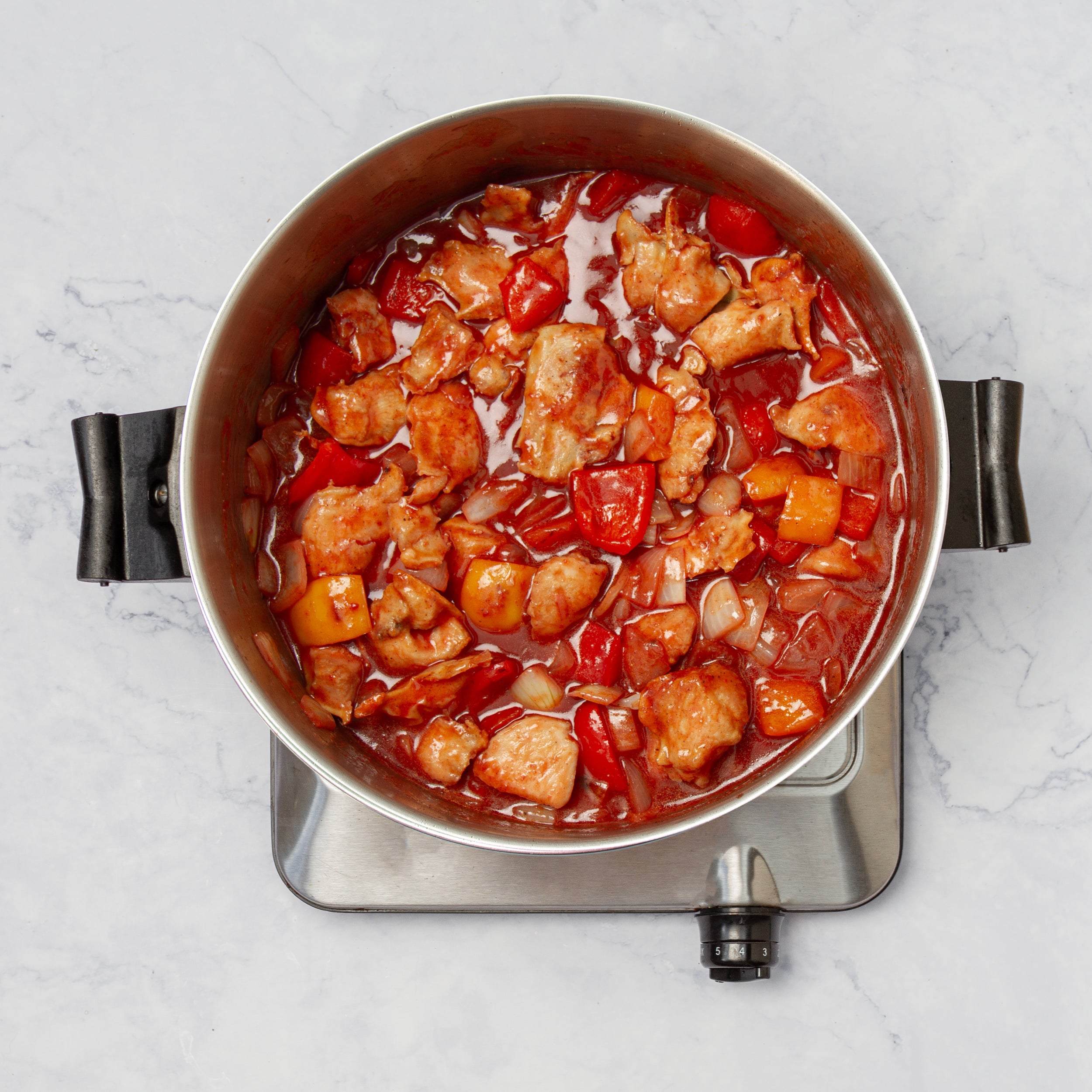 Vegetables and cooked chicken in a pot with sweet and sour sauce.