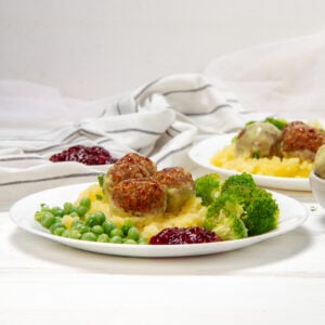 Flavorful Swedish Meatballs with creamy yogurt sauce on a plate with peas and broccoli.