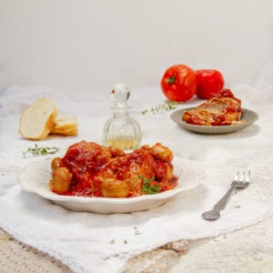 Rich and saucy Chicken Marengo on a plate with whole tomatoes and parmesan cheese on the side.