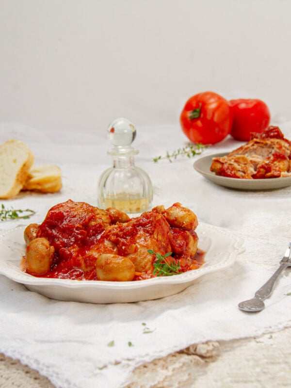 Rich and saucy Chicken Marengo on a plate with whole tomatoes and parmesan cheese on the side.