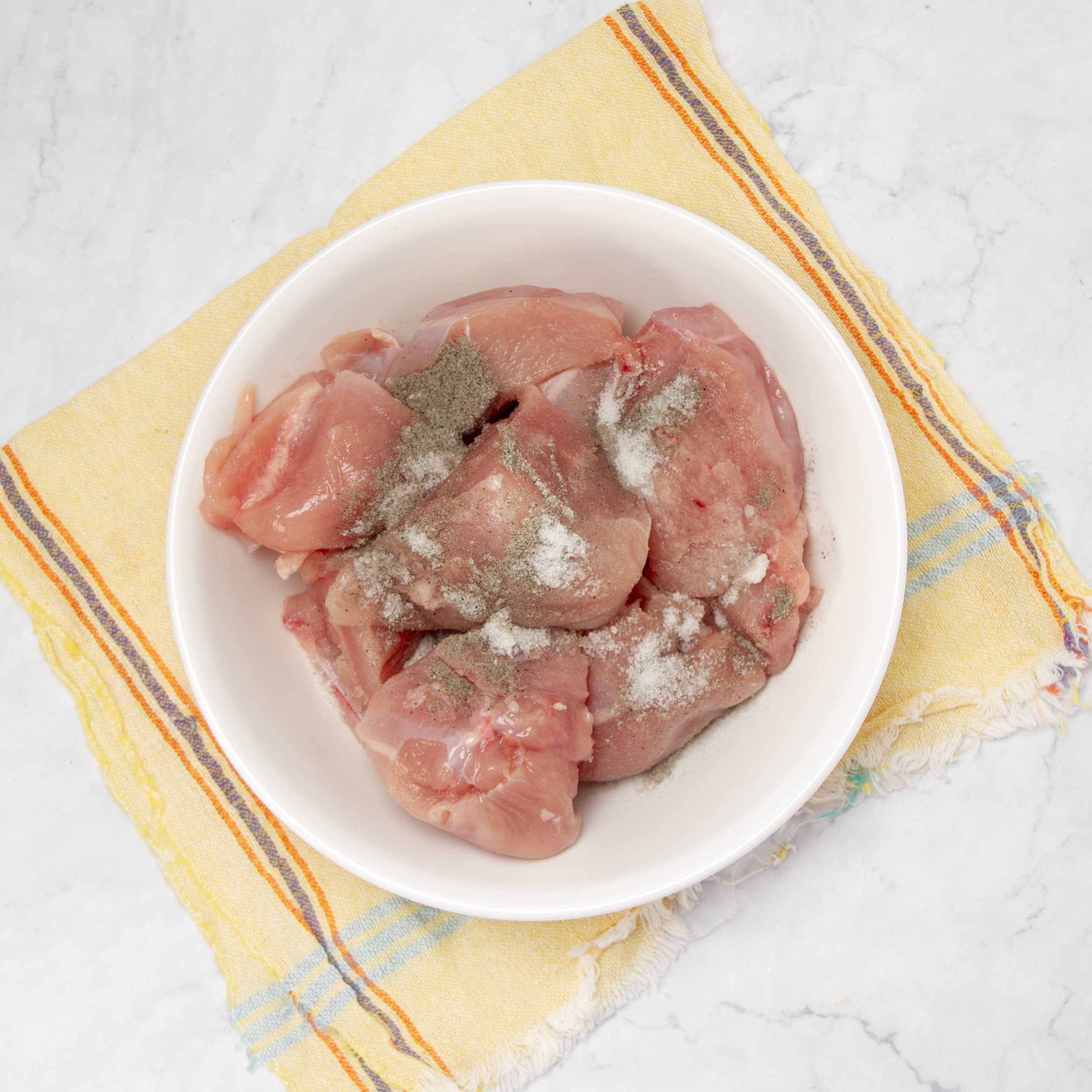 Raw chicken marinating in a small bowl.