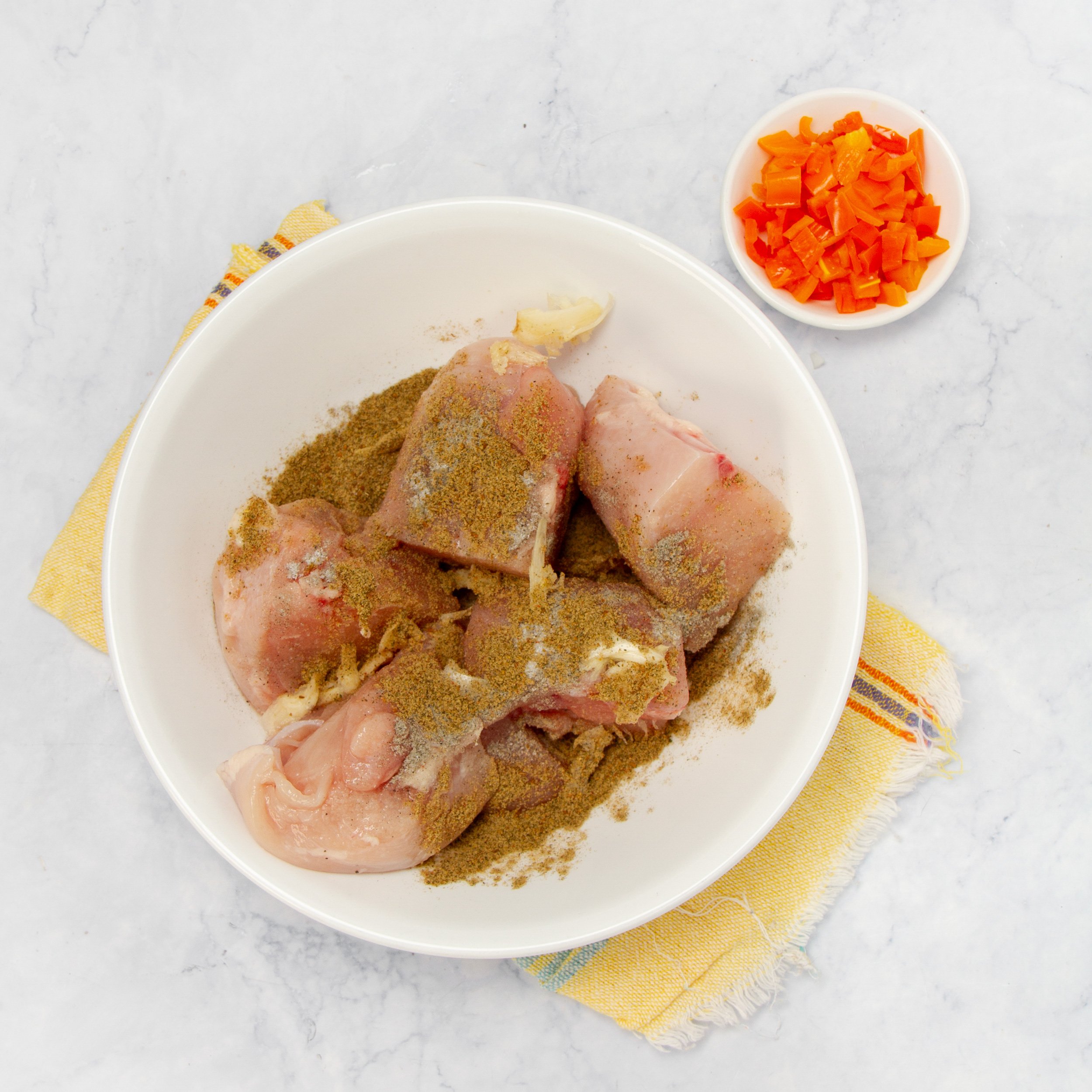 Chicken marinating with spices in a small bowl. 
