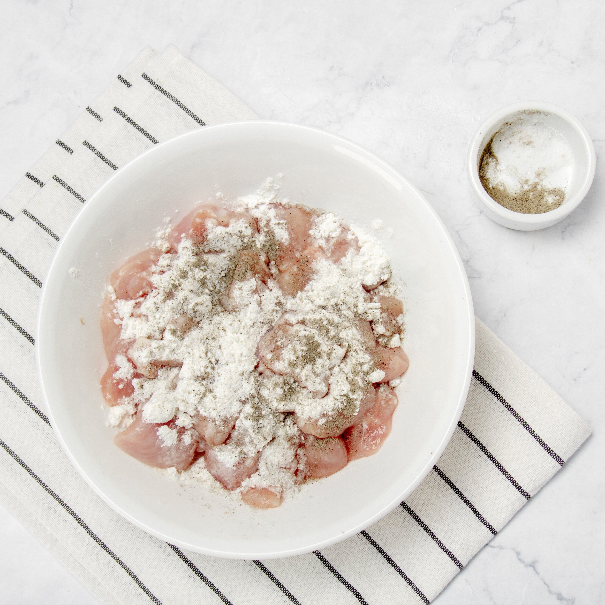 Raw chicken chunks in a small bowl, coated in flour so they crisp up nicely. 