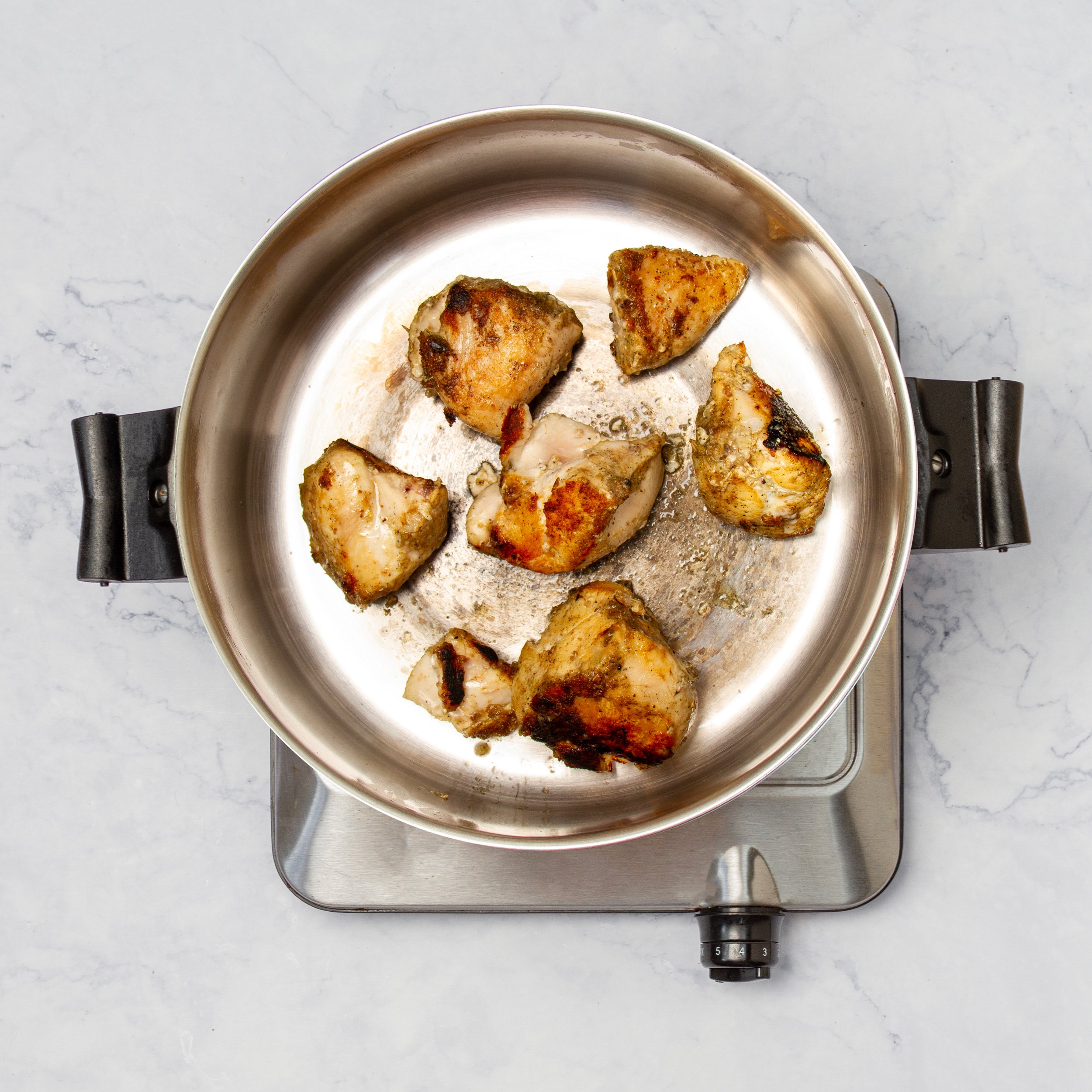 Seasoned chicken cooking in a pan. 