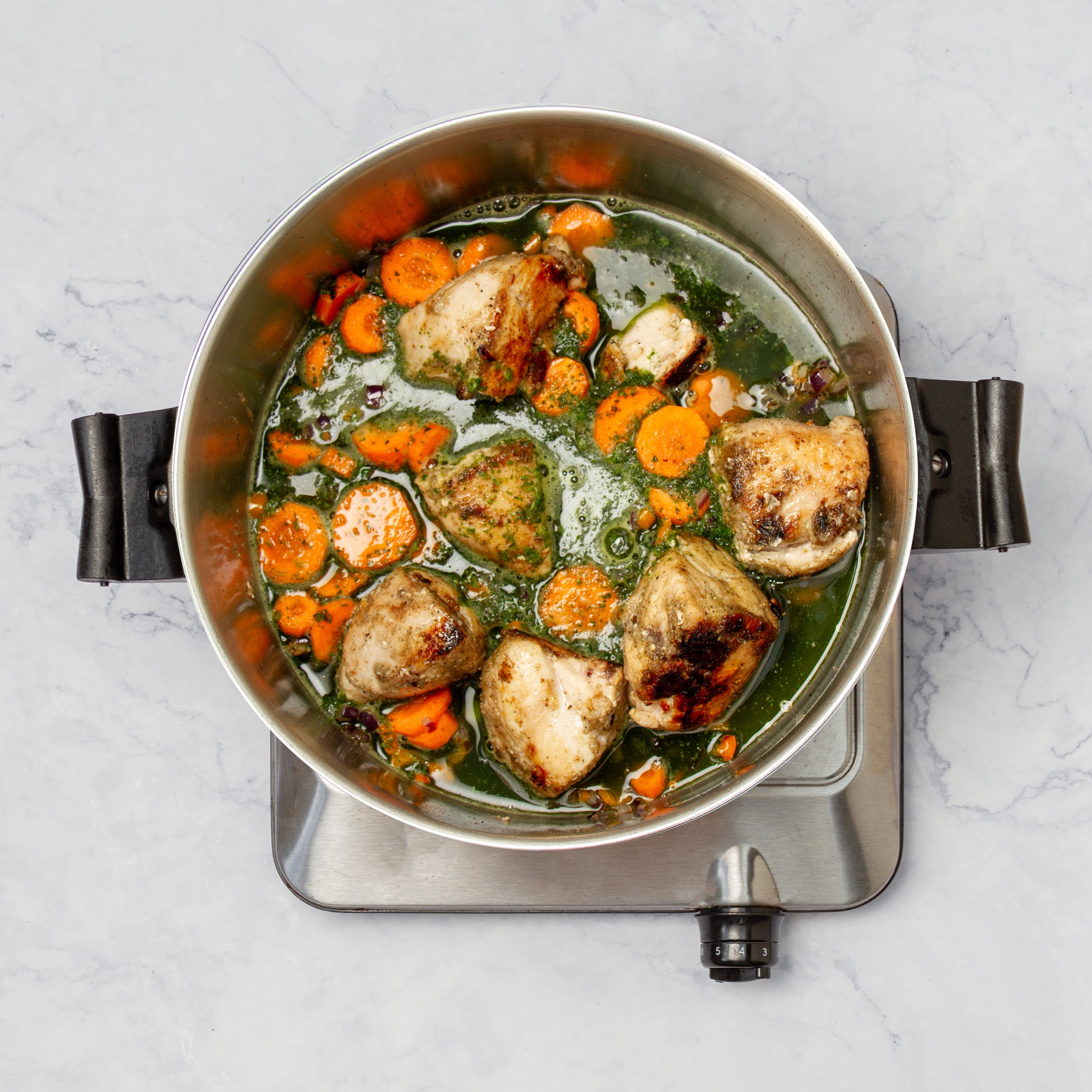 Vegetables and sauce added to the cooked chicken in a pan. 