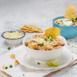 Seriously bold and satisfying Cajun white chicken chili in a bowl with tortilla chips and shredded cheese on the side.