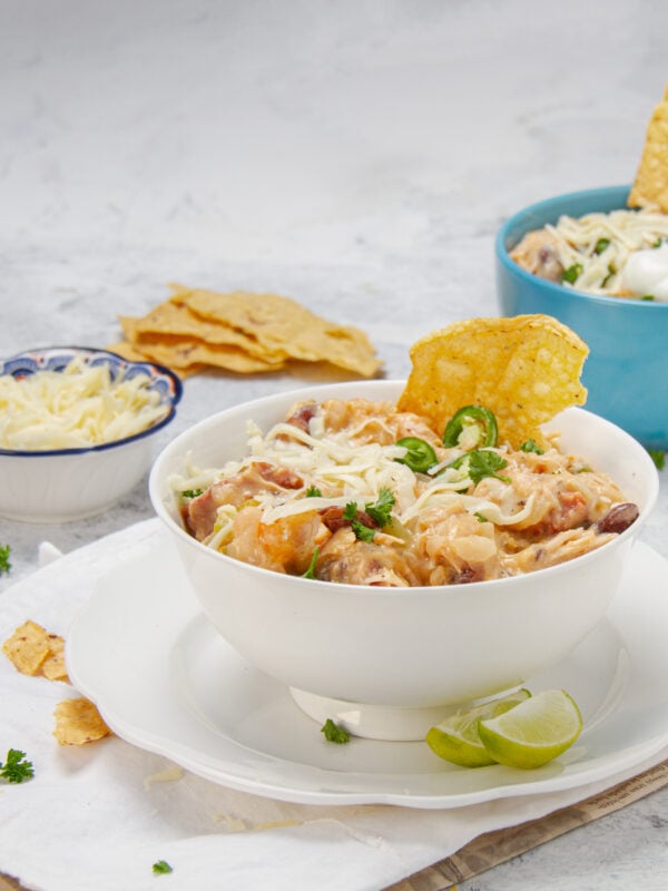 Seriously bold and satisfying Cajun white chicken chili in a bowl with tortilla chips and shredded cheese on the side.