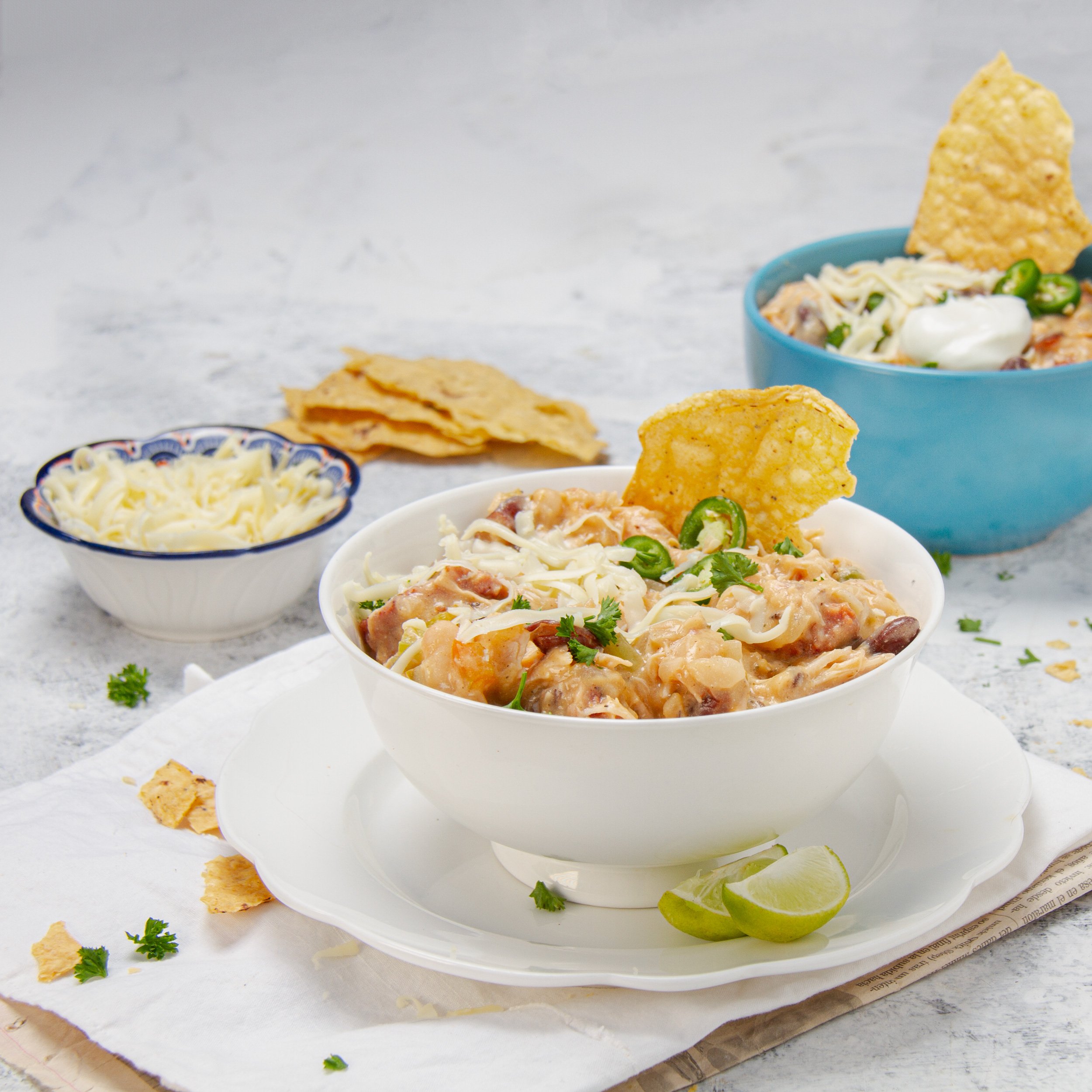 Seriously bold and satisfying Cajun white chicken chili in a bowl with tortilla chips and shredded cheese on the side.