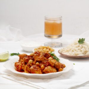 Easy and delicious chicken and chickpea curry on a plate with a cold drink and rice on the side.