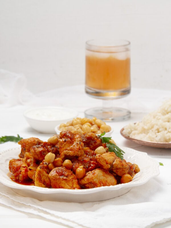 Easy and delicious chicken and chickpea curry on a plate with a cold drink and rice on the side.
