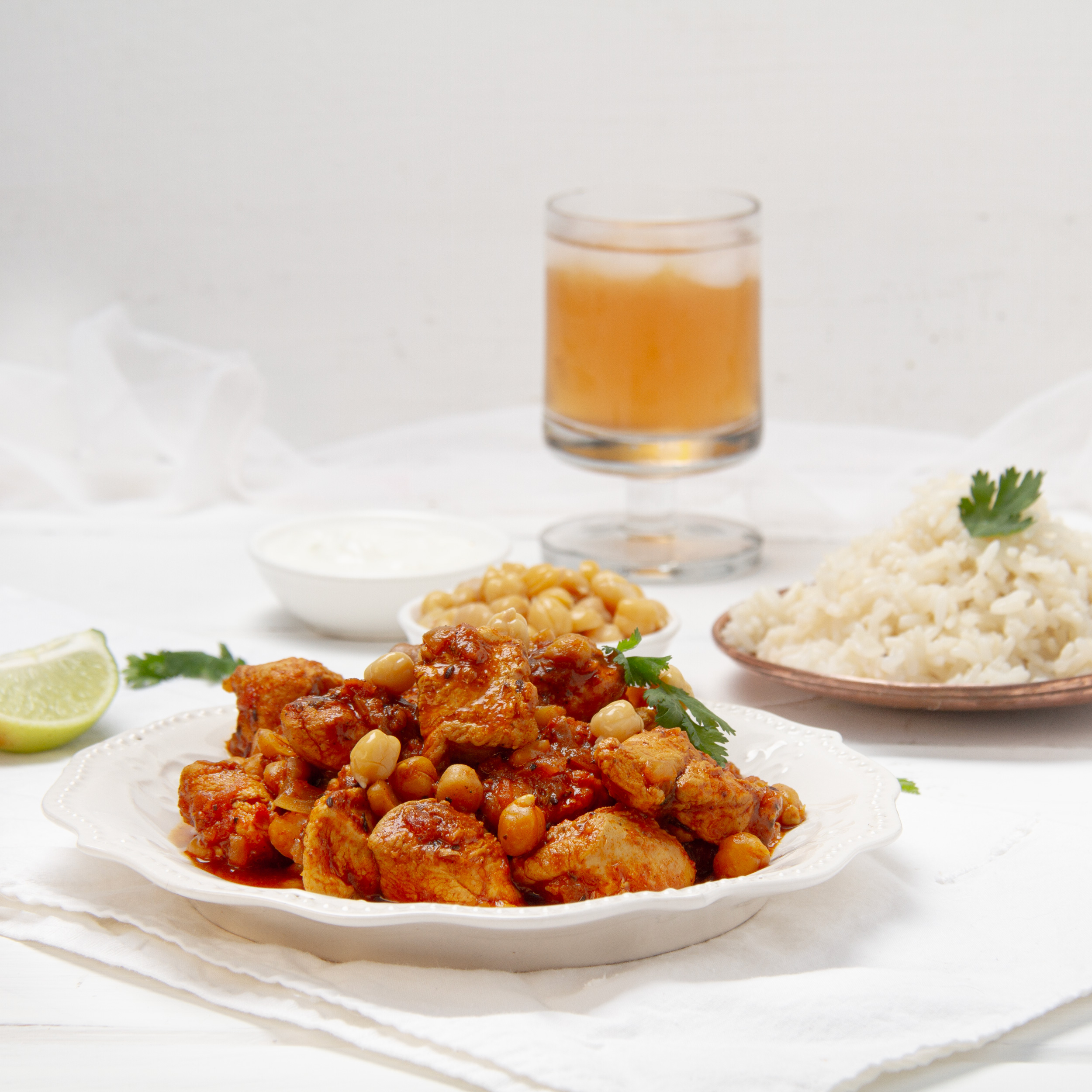 Easy and delicious chicken and chickpea curry on a plate with a cold drink and naan bread on the side.
