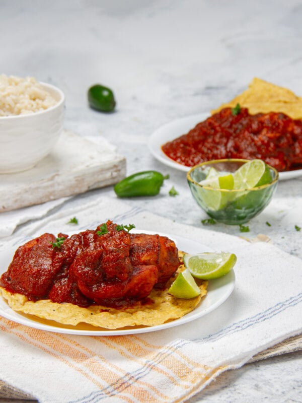 Saucy with deep flavor&mdash;Mexican Chicken Adobo on a plate with a corn tortilla and fresh lime wedges on the side.
