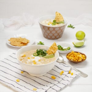 Creamy, authentic Mexican street corn soup in a bowl with chips, fresh lime wedges, and cilantro on the side.