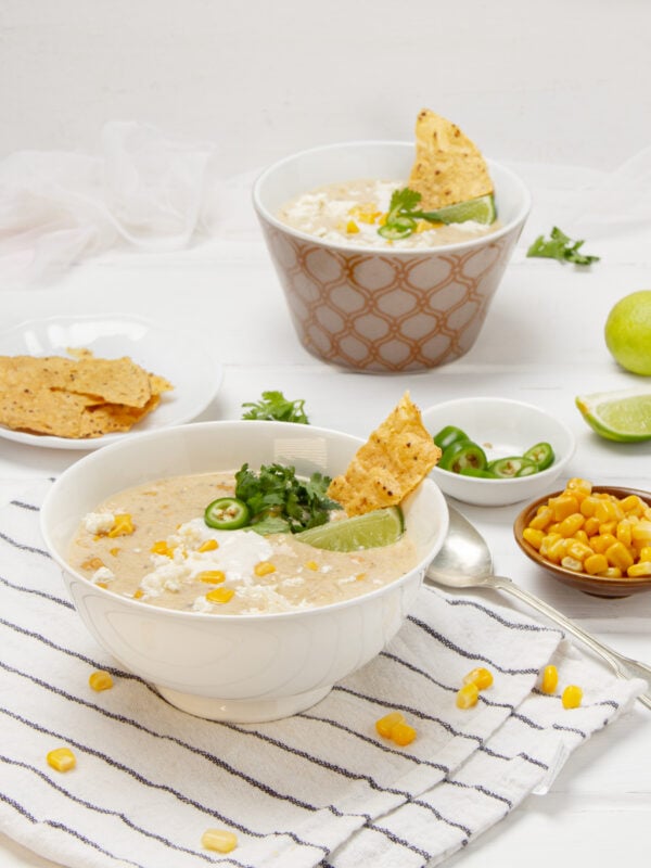 Creamy, authentic Mexican street corn soup in a bowl with chips, fresh lime wedges, and cilantro on the side.