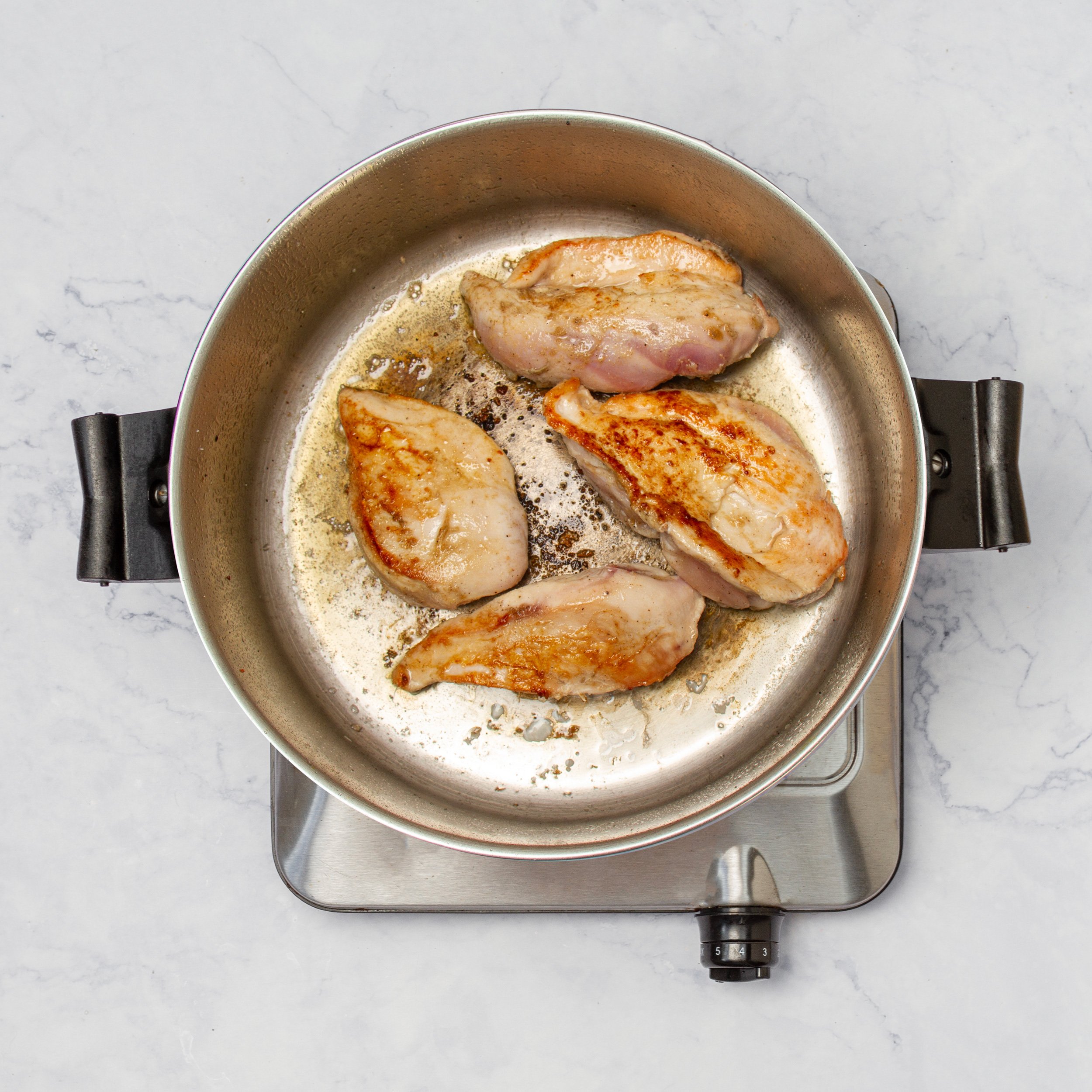 Seasoned chicken breasts cooking in a hot skillet.