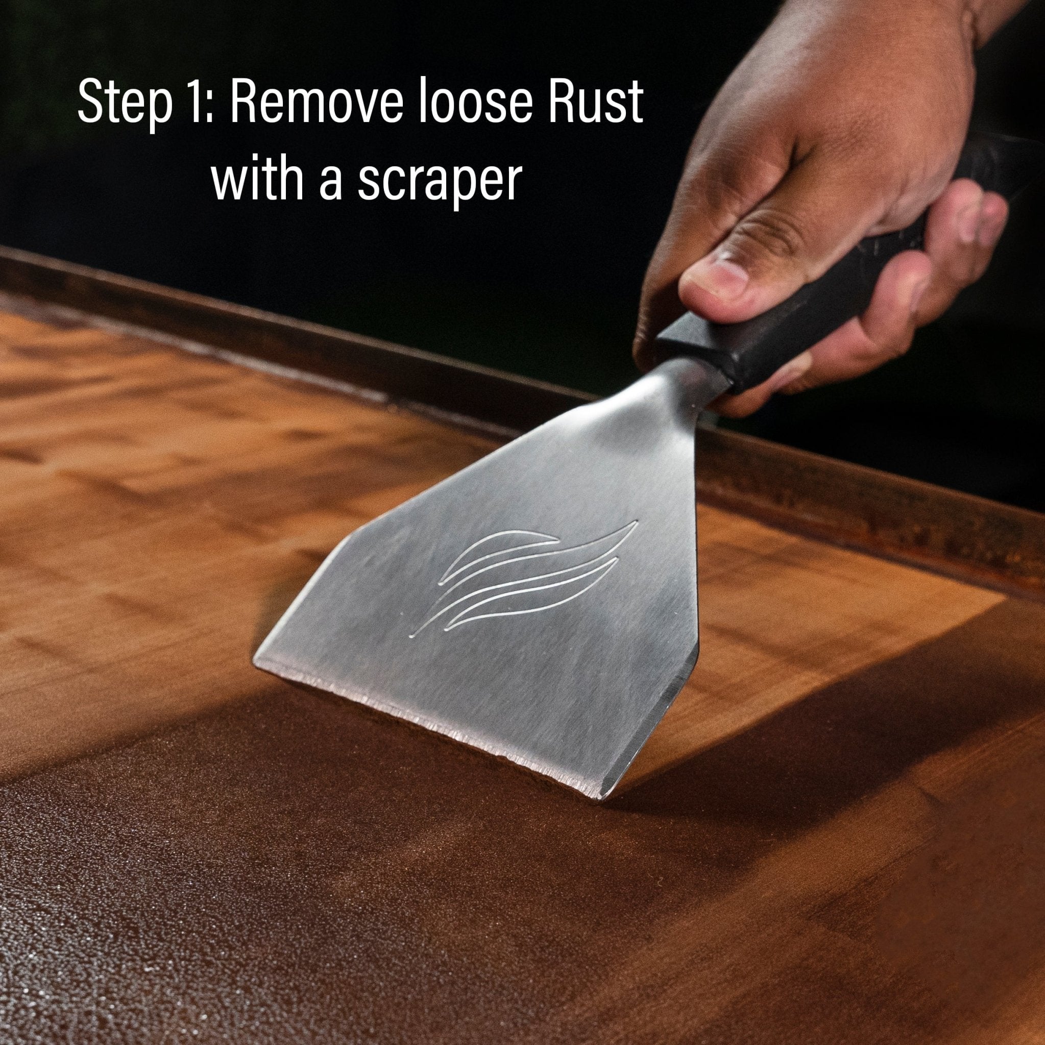 A scraper lifting rust off a griddle top, from Blackstone's restoration kit steps