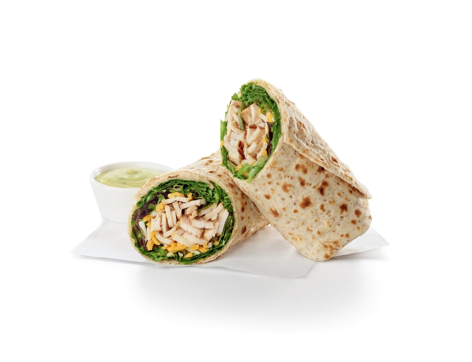 A Chick-fil-A Grilled Chicken Cool Wrap cut in half, showing sliced grilled chicken, green leaf lettuce and shredded cheese rolled in a flaxseed flatbread, with a small cup of dressing