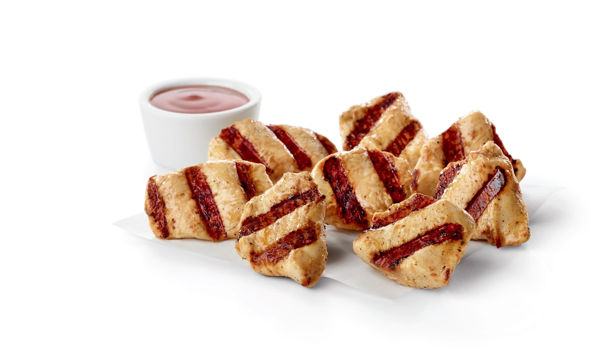 An 8-count of Chick-fil-A Grilled Nuggets with dark grill marks on white paper, next to a small white cup of dipping sauce