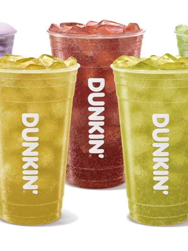 Five Dunkin' Halloween drinks in clear cups: four iced sparkling Dunkin' Zero drinks in yellow, yellow-green, bright green and dark red, and a green Sour Apple Energy topped with purple cold foam