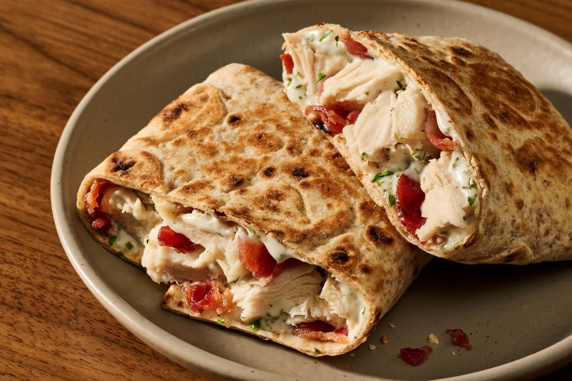A Starbucks Chicken Bacon Protein Pocket cut in half on a plate, showing chicken, bacon and garlic herb cheese spread in a toasted lavash flatbread