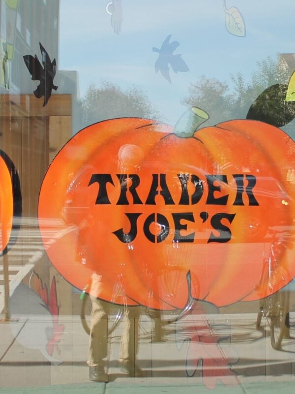 A Trader Joe's store window painted with a large orange pumpkin lettered Trader Joe's, surrounded by painted fall leaves